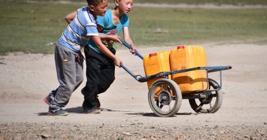 Niños transportando bidones de agua en una carretilla