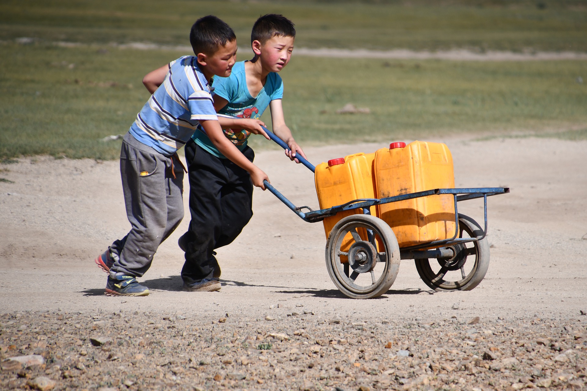 Niños transportando bidones de agua en una carretilla