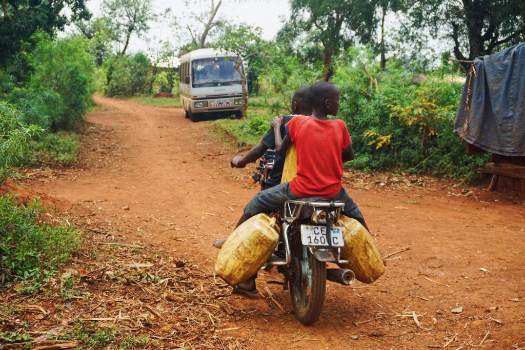 Dos jóvenes en una moto transportando bidones de agua